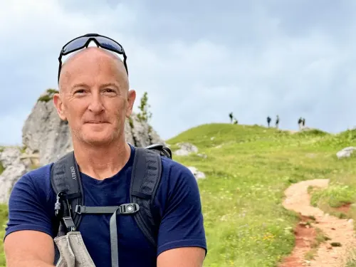 Errol Damelin hiking — navy t-shirt, Osprey backpack, green hillside.